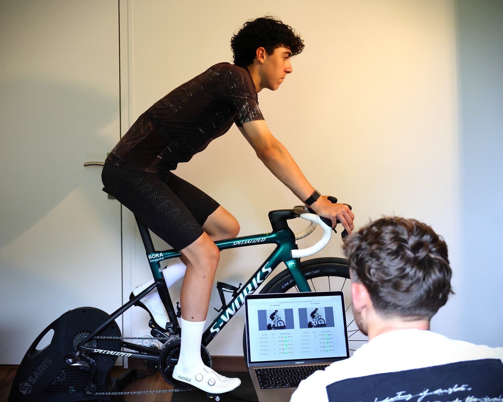 Un cycliste pédale sur home-trainer pendant une étude posturale, l'analyse affichée à l'écran